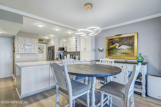 dining area with sink, light hardwood / wood-style flooring, a chandelier, and ornamental molding