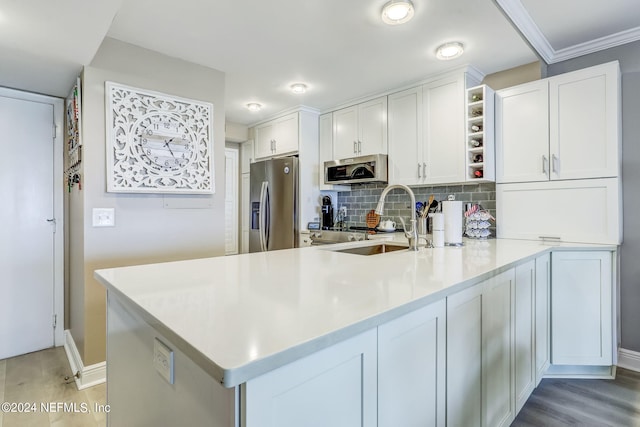 kitchen featuring kitchen peninsula, backsplash, stainless steel appliances, sink, and white cabinetry