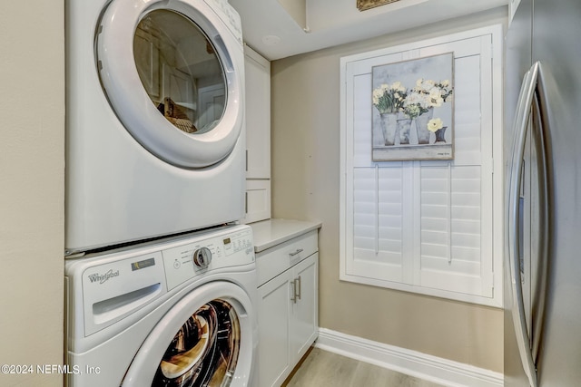 laundry room with light hardwood / wood-style floors, cabinets, and stacked washer / dryer