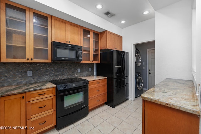 kitchen with light stone countertops, backsplash, black appliances, light tile patterned floors, and stacked washer and clothes dryer