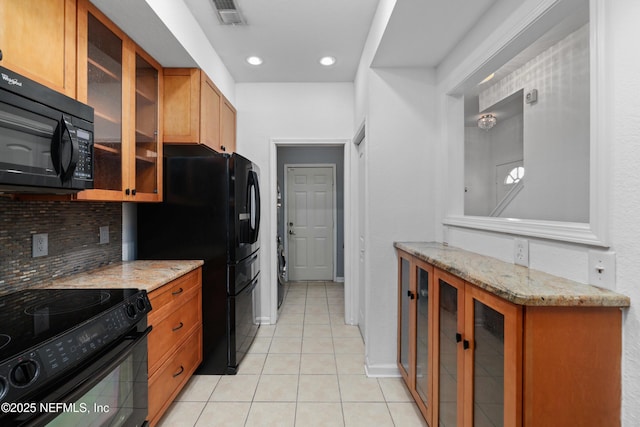 kitchen with light tile patterned floors, tasteful backsplash, light stone counters, and black appliances