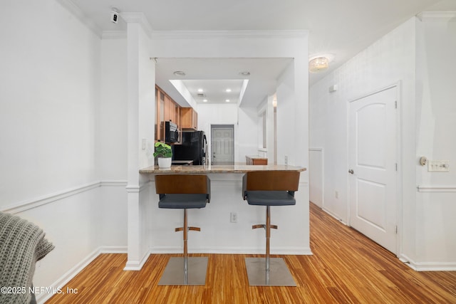 kitchen featuring kitchen peninsula, a kitchen breakfast bar, light hardwood / wood-style floors, and black fridge