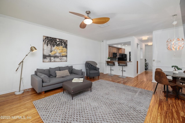 living room featuring hardwood / wood-style floors, ceiling fan with notable chandelier, and ornamental molding