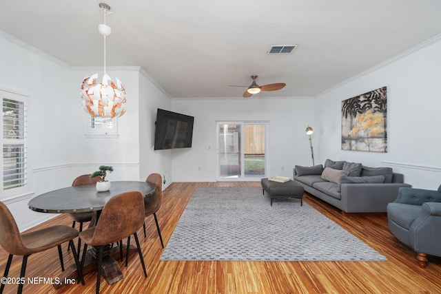 living room featuring ceiling fan with notable chandelier, wood-type flooring, and crown molding