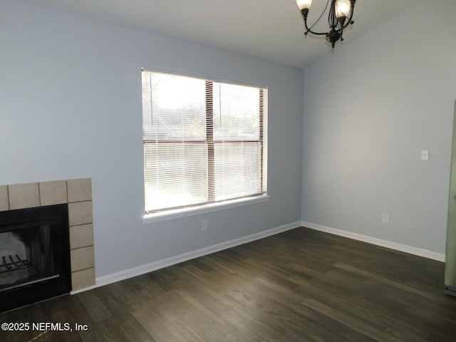 unfurnished living room with a tile fireplace, dark wood-type flooring, and a notable chandelier