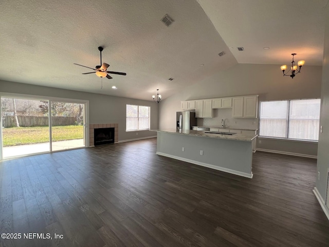 unfurnished living room featuring plenty of natural light, ceiling fan with notable chandelier, dark wood-type flooring, and a tile fireplace