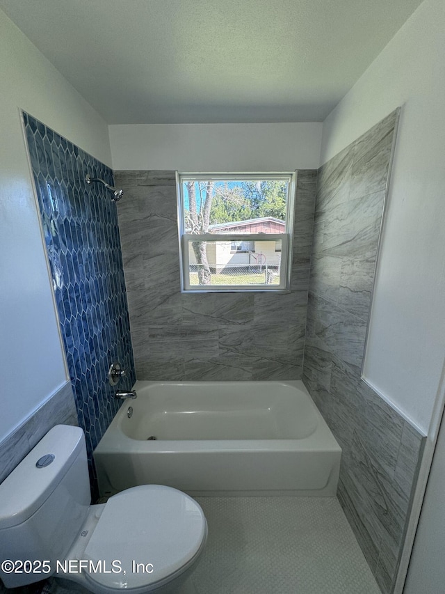 bathroom featuring tile patterned flooring, tiled shower / bath combo, toilet, and tile walls