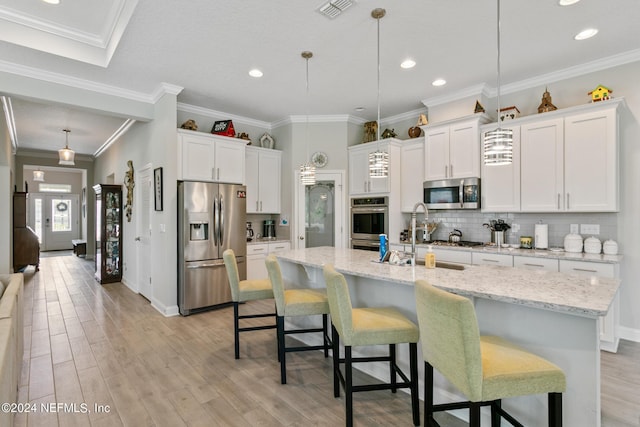 kitchen with a center island with sink, white cabinets, hanging light fixtures, and appliances with stainless steel finishes