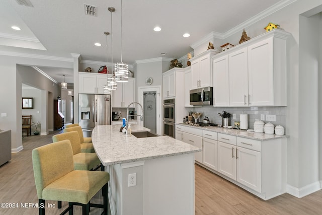 kitchen with a kitchen island with sink, white cabinets, sink, tasteful backsplash, and stainless steel appliances