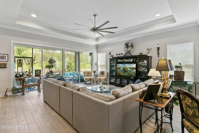 living room with a raised ceiling, ceiling fan, and crown molding