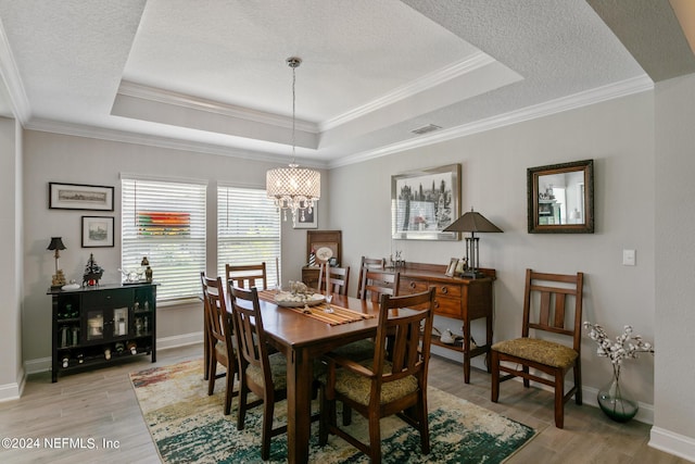 dining area with a tray ceiling, crown molding, light hardwood / wood-style flooring, and a chandelier