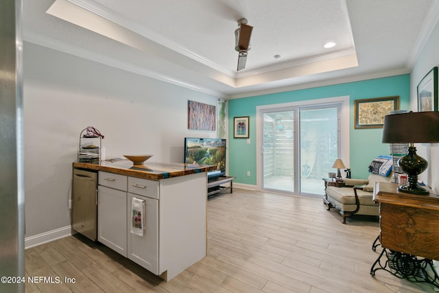 kitchen with white cabinets, light wood-type flooring, a raised ceiling, and crown molding