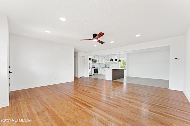 unfurnished living room featuring ceiling fan, light wood-type flooring, and sink