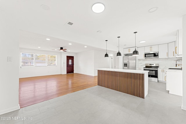 kitchen featuring appliances with stainless steel finishes, ceiling fan, decorative light fixtures, a center island, and white cabinetry