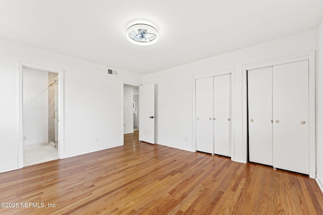 unfurnished bedroom with connected bathroom, multiple closets, and light hardwood / wood-style flooring