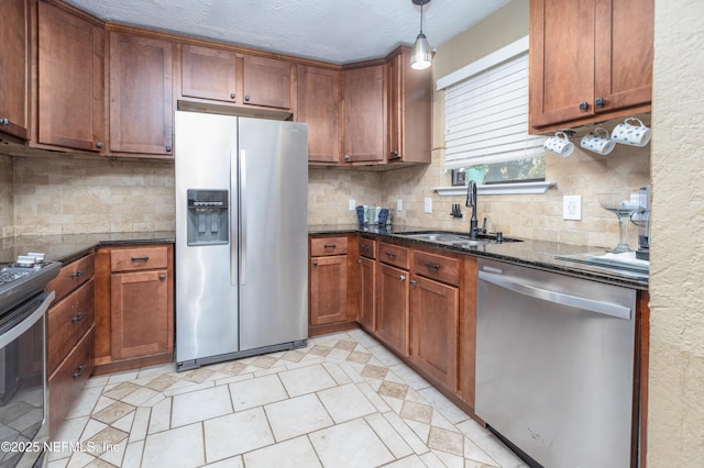 kitchen featuring sink, hanging light fixtures, stainless steel appliances, dark stone counters, and a textured ceiling