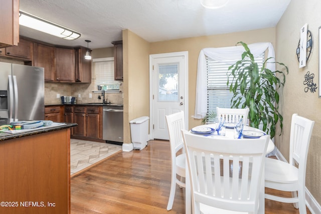 kitchen featuring sink, stainless steel appliances, backsplash, pendant lighting, and wood-type flooring