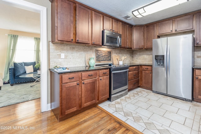 kitchen featuring backsplash, light hardwood / wood-style flooring, dark stone countertops, a textured ceiling, and appliances with stainless steel finishes