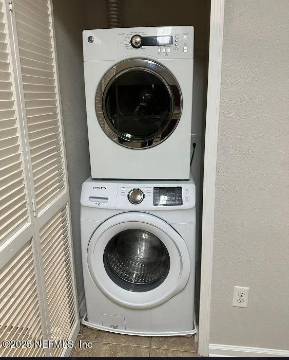 clothes washing area with tile patterned floors and stacked washer / drying machine