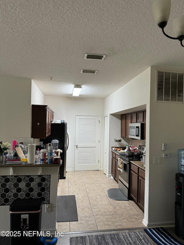 kitchen with a textured ceiling, dark brown cabinets, light tile patterned floors, and stainless steel appliances