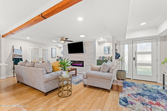 living room with ceiling fan, french doors, light hardwood / wood-style flooring, a fireplace, and ornamental molding