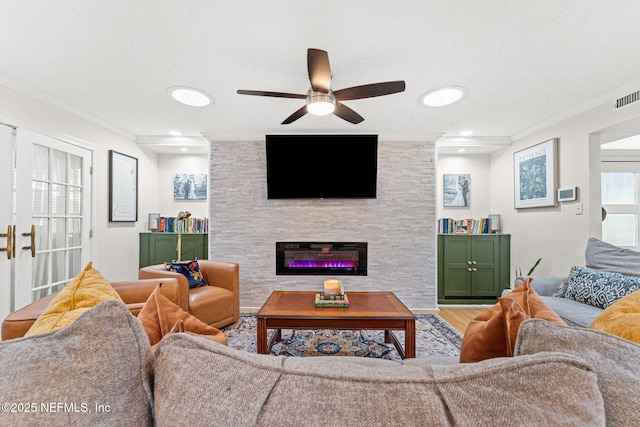 living room featuring hardwood / wood-style floors, ceiling fan, ornamental molding, a textured ceiling, and a large fireplace