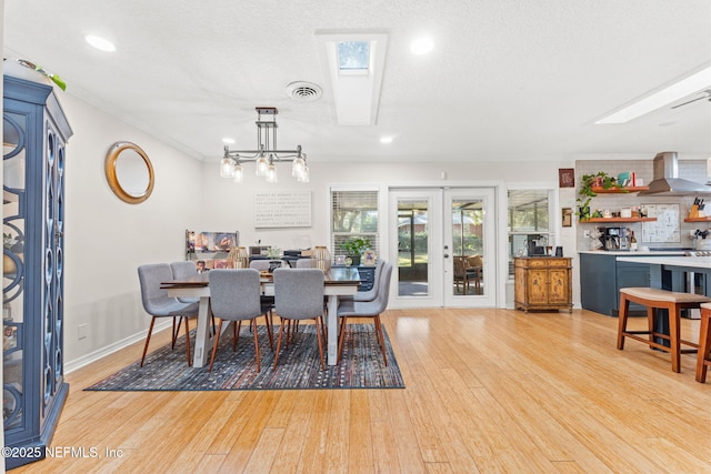 dining area with french doors, a skylight, a textured ceiling, crown molding, and light hardwood / wood-style flooring