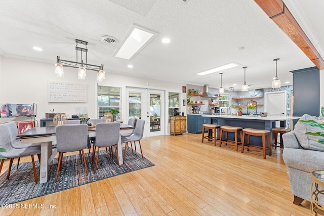 dining room with crown molding, french doors, a textured ceiling, and light wood-type flooring