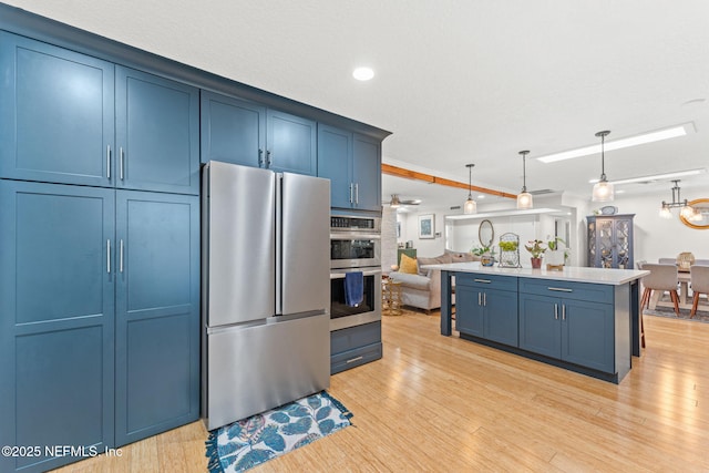 kitchen with a kitchen island with sink, blue cabinets, hanging light fixtures, light wood-type flooring, and stainless steel appliances