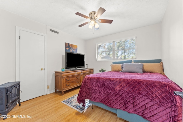 bedroom with hardwood / wood-style flooring, ceiling fan, and a wood stove