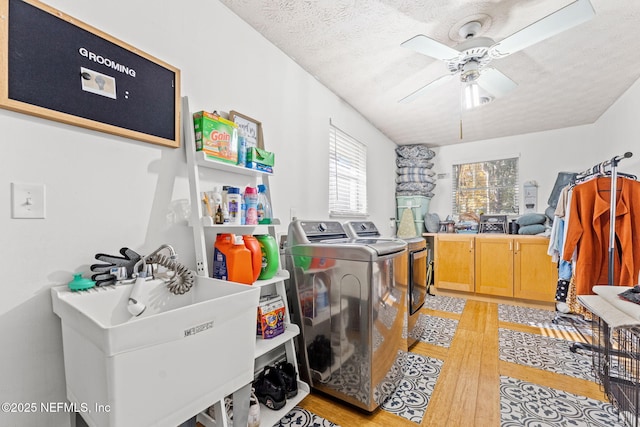 laundry area with light wood-type flooring, a textured ceiling, ceiling fan, sink, and washing machine and clothes dryer