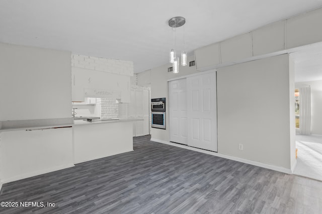 kitchen featuring dark wood-type flooring, hanging light fixtures, kitchen peninsula, double oven, and white cabinets