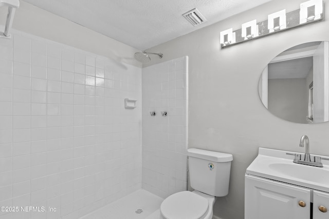 bathroom featuring vanity, a textured ceiling, toilet, and a tile shower