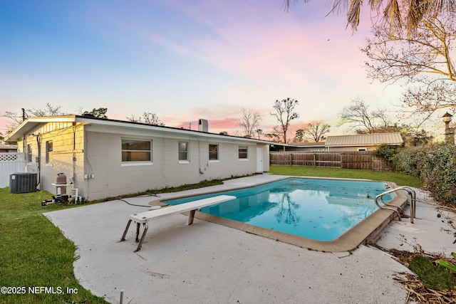 pool at dusk featuring central AC, a patio area, and a lawn