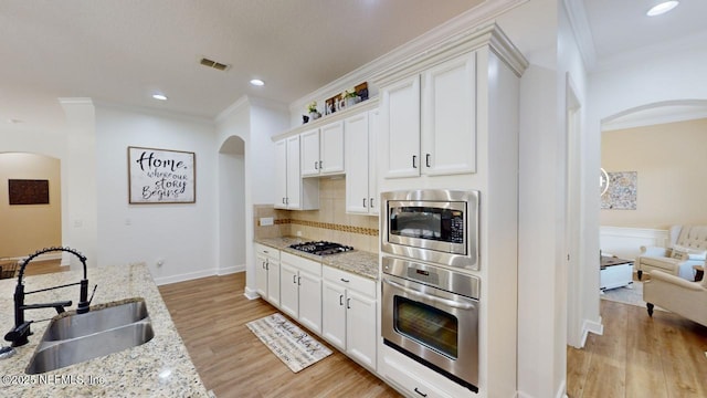 kitchen featuring light stone countertops, sink, stainless steel appliances, white cabinets, and ornamental molding