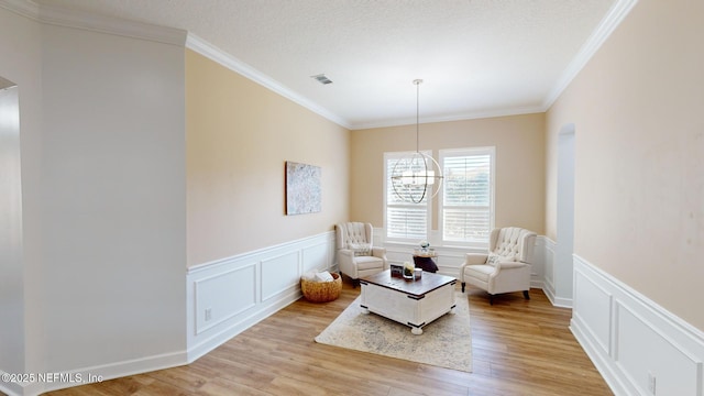 living area with light wood-type flooring, ornamental molding, a textured ceiling, and a chandelier