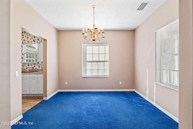 carpeted empty room featuring a notable chandelier and a textured ceiling