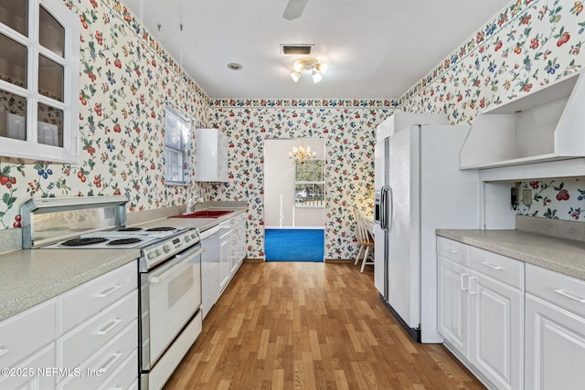 kitchen featuring sink, white appliances, a notable chandelier, white cabinets, and light wood-type flooring