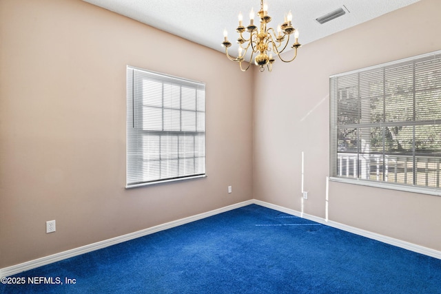 carpeted empty room with a textured ceiling and a chandelier