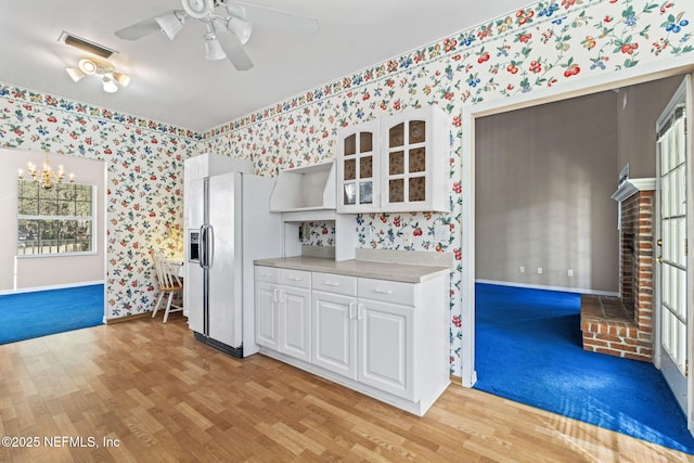 kitchen featuring ceiling fan with notable chandelier, white refrigerator with ice dispenser, light hardwood / wood-style floors, and white cabinets