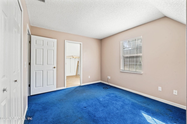 unfurnished bedroom featuring ensuite bathroom, dark carpet, and a textured ceiling