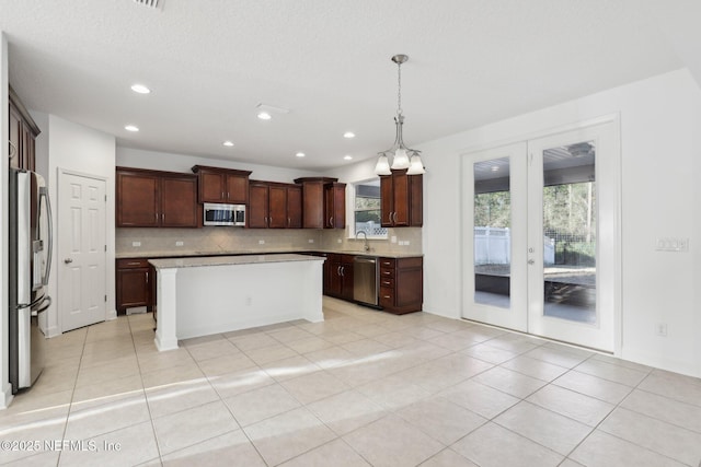 kitchen with appliances with stainless steel finishes, french doors, sink, pendant lighting, and a kitchen island