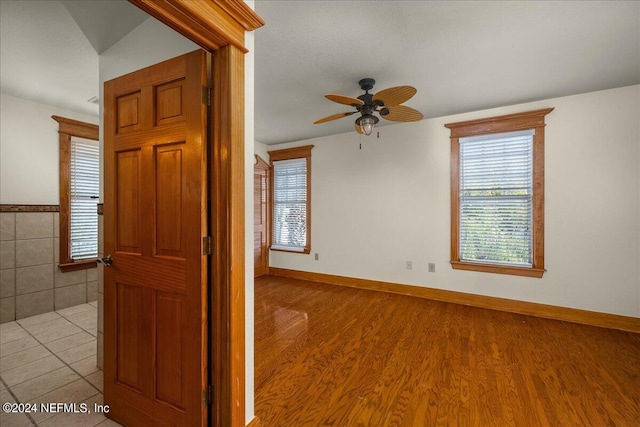 spare room featuring light hardwood / wood-style flooring, ceiling fan, and tile walls