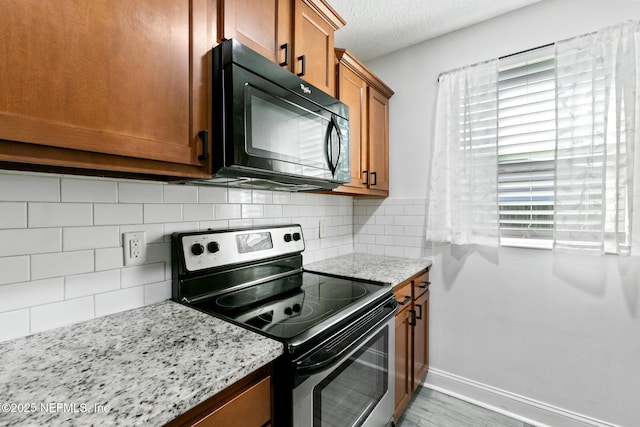 kitchen featuring tasteful backsplash, stainless steel electric range, light stone countertops, a textured ceiling, and light hardwood / wood-style flooring