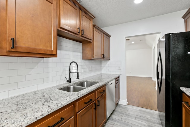 kitchen featuring black refrigerator, sink, backsplash, light stone counters, and stainless steel dishwasher