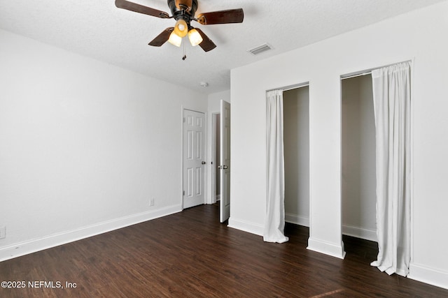 unfurnished bedroom with ceiling fan, a textured ceiling, dark hardwood / wood-style flooring, and multiple closets