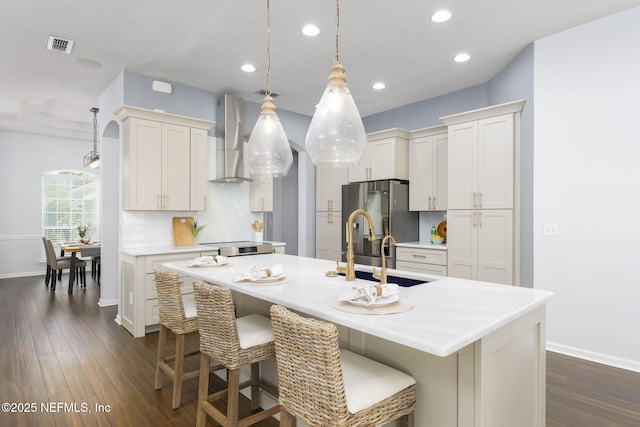 kitchen with sink, white cabinets, hanging light fixtures, a kitchen island with sink, and wall chimney range hood