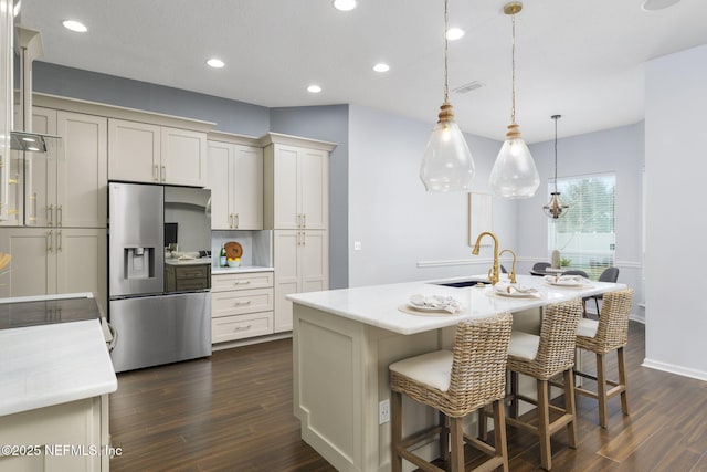 kitchen featuring dark wood-type flooring, sink, decorative light fixtures, stainless steel fridge with ice dispenser, and an island with sink