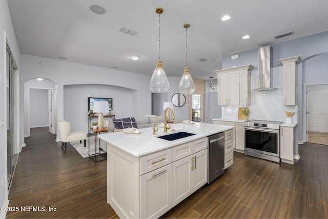 kitchen featuring sink, appliances with stainless steel finishes, white cabinetry, a kitchen island with sink, and wall chimney exhaust hood