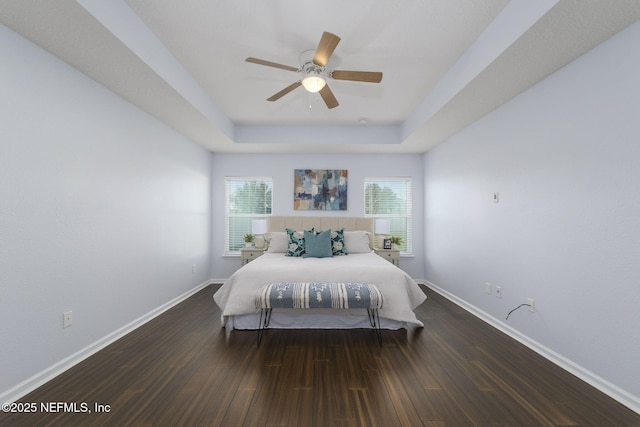 bedroom featuring a raised ceiling, dark wood-type flooring, and ceiling fan